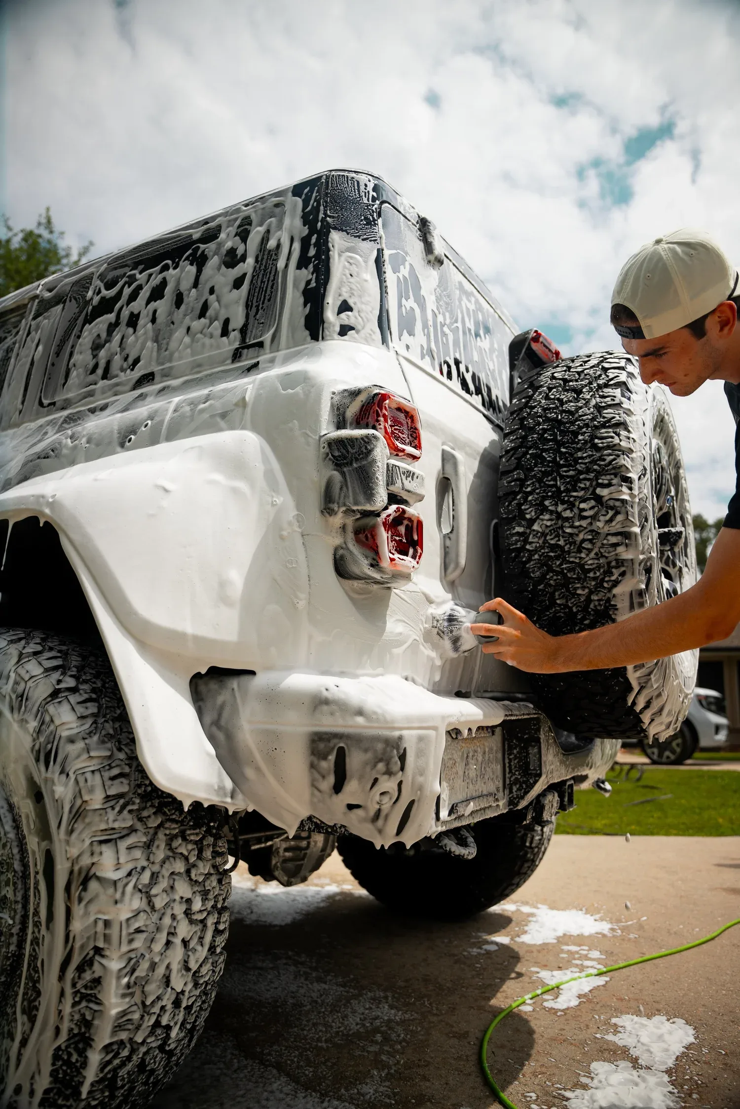 Detailer foam-washing the rear of a white off-road SUV in a driveway